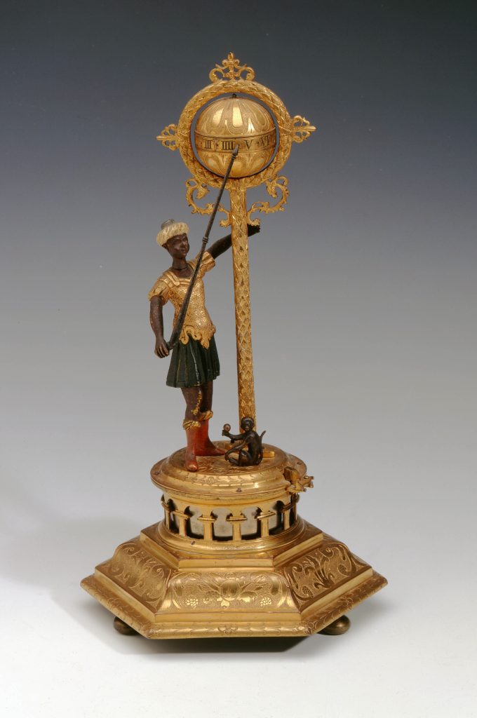 Brass figure clock, featuring an African man, in Roman dress, pointing to the hour.